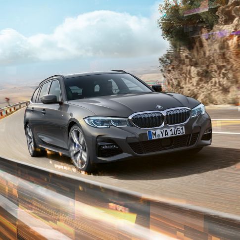斜め前から写した BMW 3 シリーズ ツーリングのデザイン G21 田舎の景色を背景に、橋の上を走行している姿を斜め前から写した BMW 3 シリーズ ツーリング G21