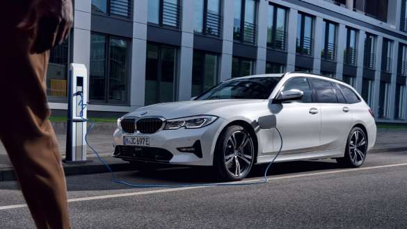 BMW 3シリーズ ツーリング 2021 G21 プラグイン・ハイブリッド 斜めからのフロント・ビュー 充電中 BMW 3シリーズ ツーリング 2021 G21 プラグイン・ハイブリッド 斜めからのフロント・ビュー 建物の前で充電中