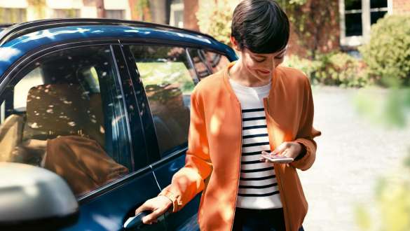 女性がスマートフォンを見ながらBMWのドアを開ける BMWテレサービス 女性がスマートフォンを見ながらBMWのドアを開ける