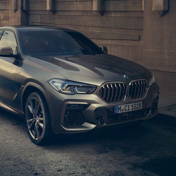 停車中の BMW X6 M50i。G06 市街地を背景に停車する BMW X6 M50i のスリークウォーター・フロントビュー。G06