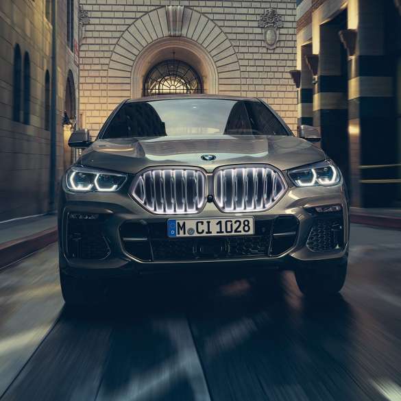 BMW キドニー・グリル「アイコニック・グロウ」を備える BMW X6 M50i。G06 市街地を背景に停車する BMW X6 M50i のフロントビュー。G06