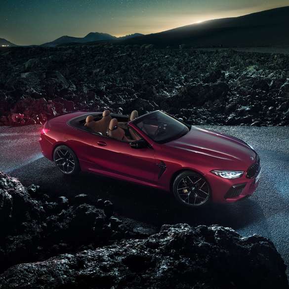 BMW M8 Competition カブリオレ、スリークウォーター・サイドビュー。F91 BMW M8 Competition カブリオレのモテギ・レッド・メタリックカラー (ソフトトップを開けた状態)、夜のアスファルト上でのスリークウォーター・サイドビュー。F91