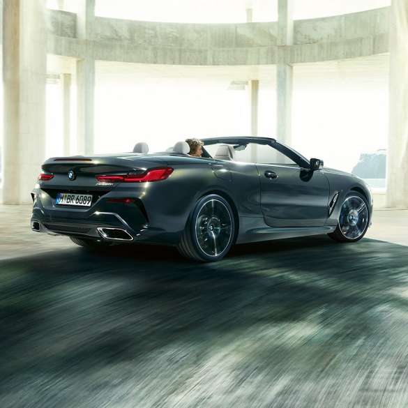 BMW M850i xDrive カブリオレ、スリークウォーター・リアビュー。G14 BMW M850i xDrive カブリオレのドラバイト・グレー・メタリックカラー (ソフトトップを開けた状態) 、コンクリートのビル内を走り抜けている時のスリークウォーター・リアビュー。G14