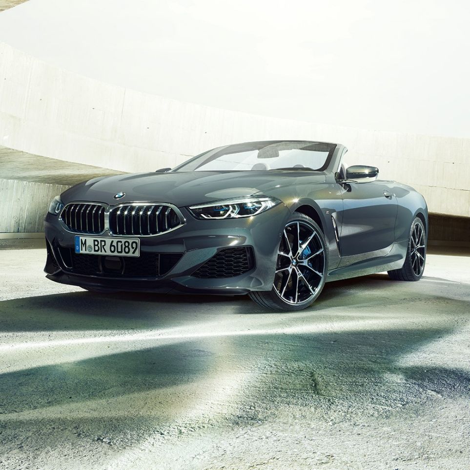 BMW M850i xDrive カブリオレ、スリークォータービュー。G14 BMW M850i xDrive カブリオレのドラバイト・グレー・メタリックカラー (ソフトトップを開けた状態)、コンクリートのビル内でのスリークォータービュー。G14