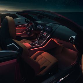 BMW M8 Competition カブリオレ、インテリア。F91 BMW M8 Competition カブリオレ (ソフトトップを開けた状態)、赤いアンビエントライトが光る夜間のインテリア。F91