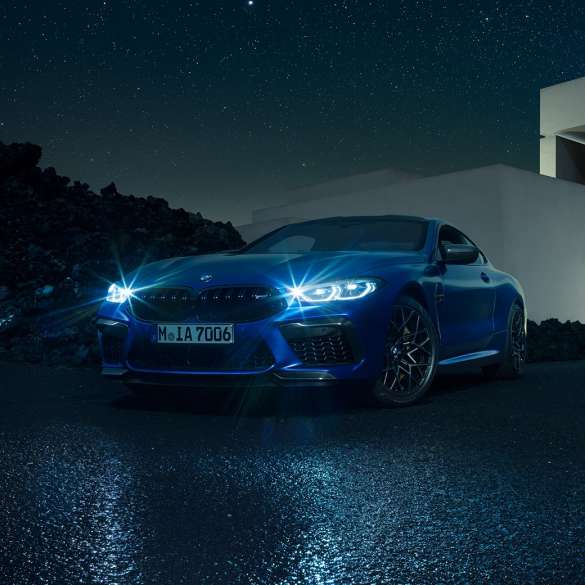 BMW M8 コンペティションクーペ、スリークォーターフロントビュー。F92 BMW M8 コンペティションクーペ(塗色マリーナベイ ブルーメタリック)。邸宅の前に停車中。きらめくLEDヘッドライトが印象的なスリークォーターフロントビュー。F92