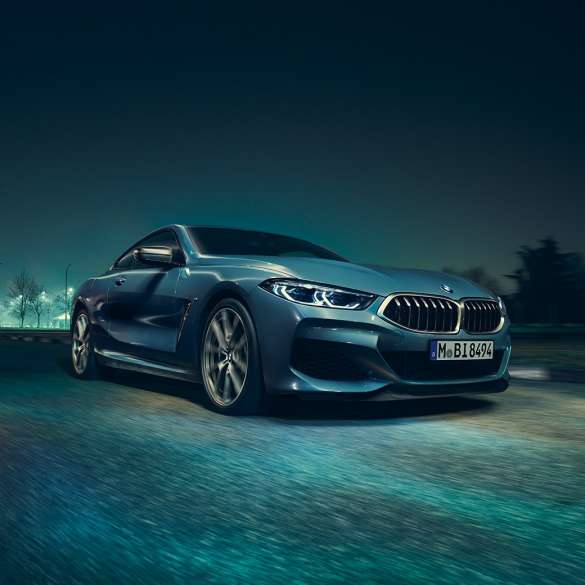 BMW M850i xDriveクーペ、左側から捉えたスリークォーターフロントビュー。G15 BMW M850i xDriveクーペ(塗色バルセロナ ブルーメタリック)。夜間に疾走する車両を左側から捉えたスリークォーターフロントビュー。G15