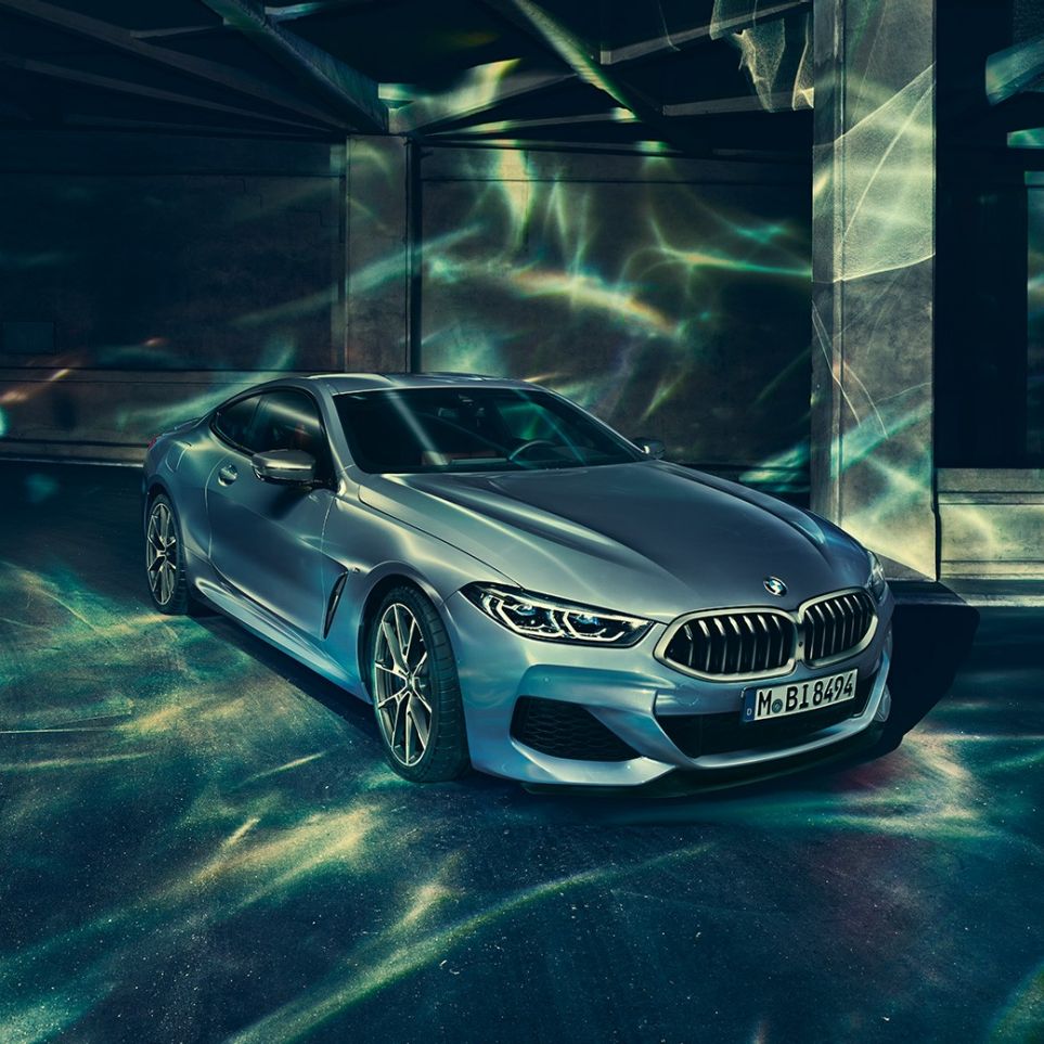 BMW M850i xDriveクーペ、左側からのスリークォーターフロントビュー。G15 BMW M850i xDriveクーペ(塗色バルセロナ ブルーメタリック)。ビルの前に停車した左側からのスリークォーターフロントビュー。G15