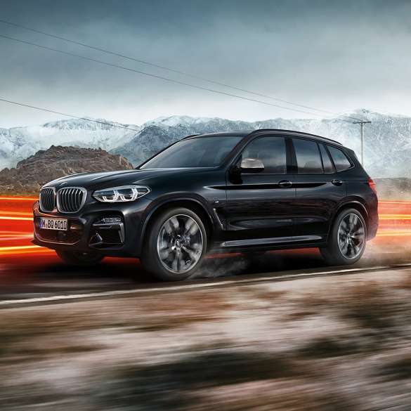 BMW X3 M40d、サイドビュー。F97 BMW X3 M40d のブラック・サファイア・メタリックカラー、走行中、エクステリア、山の風景をバックにライトを点灯させているサイドビュー。F97