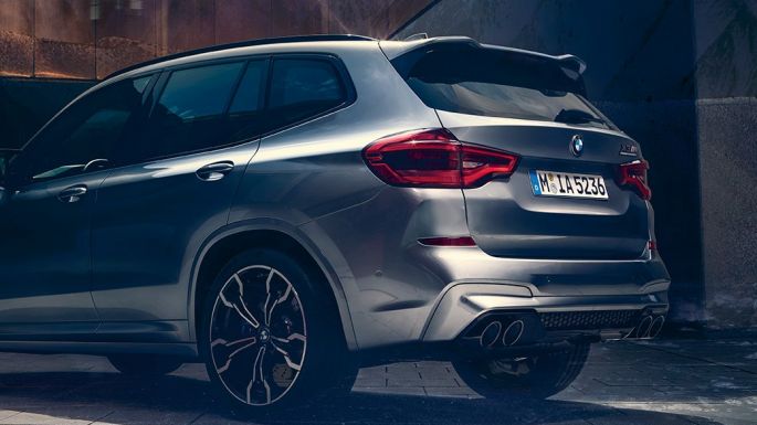 BMW X3 M Competition、斜めリアビュー。F97 BMW X3 M Competitionのドニントン・グレー・メタリックカラー、エクステリア、前景に2人の人間が立っている斜めリアビュー。F97