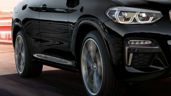 BMW X4 M40i、斜め向きサイド・ビュー。 ブラック・サファイア・メタリックのBMW X4 M40i、走行中、エクステリア、回転するライト・アロイ・ホイールの見える斜め向きサイド・ビュー。