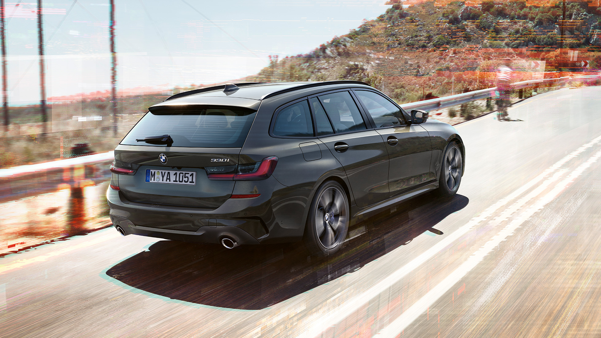 斜め後ろから写した BMW 3 シリーズ ツーリング G21 田舎の景色を背景に、橋の上を走行している姿を斜め後ろから写した BMW 3 シリーズ ツーリング G21