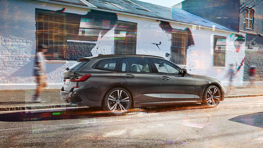 BMW 3シリーズ ツーリング(G21)、ドラバイト・グレー、やや斜めからのリヤ・ビュー BMW 3シリーズ ツーリング(G21)、ドラバイト・グレー、建物の前で走行中、やや斜めからのリヤ・ビュー