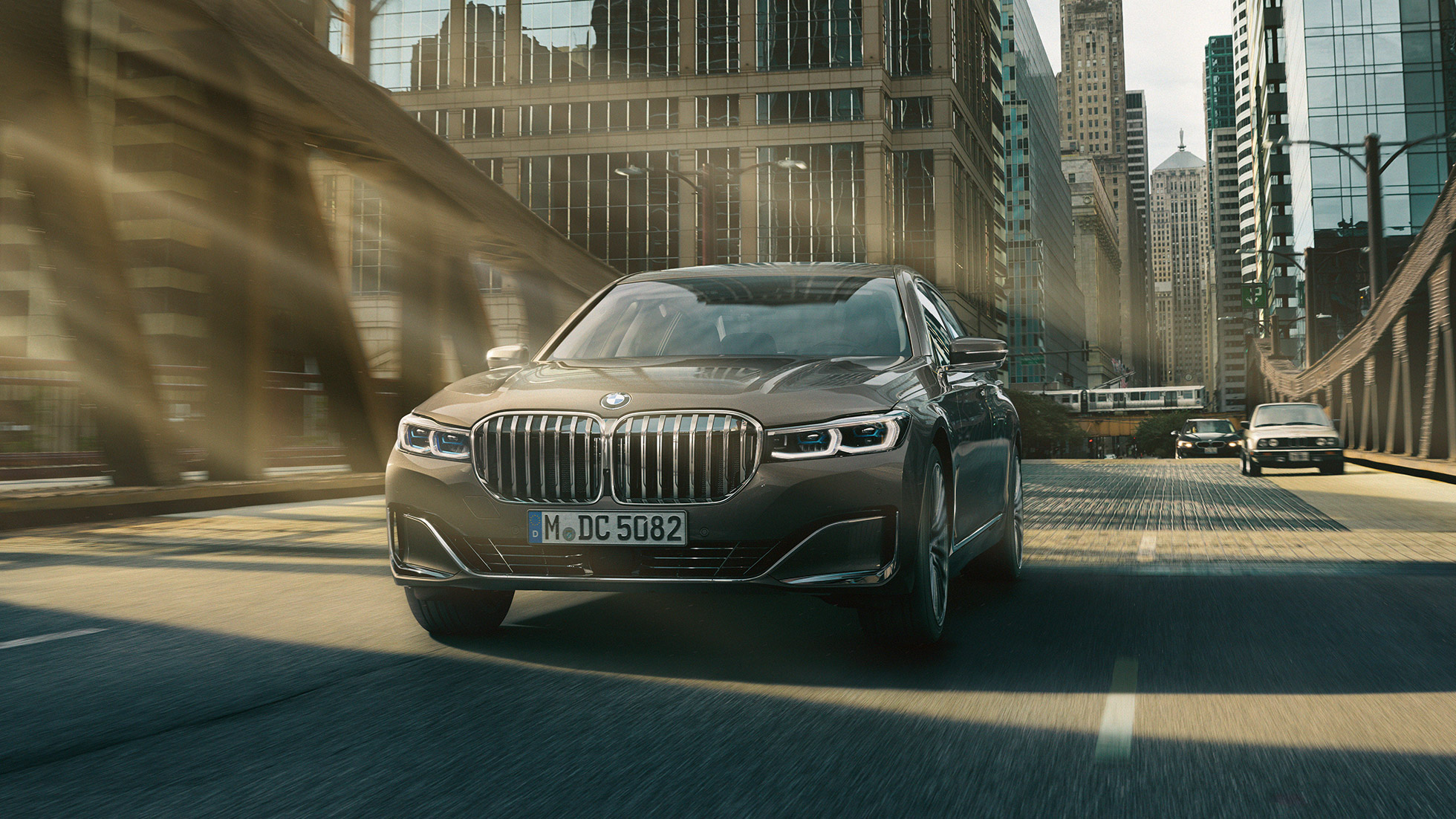 BMW 7 シリーズ セダンのドライビング・アシスト・システム ドライビング・アシスト・システム:都市風景を背に走行するBMW 7 シリーズ セダン