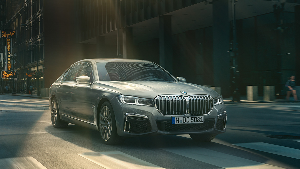 BMW 7 シリーズ セダンのドライビング・アシスト・プロフェッショナル G11 ドライビング・アシスト・プロフェッショナル:都市風景を背に走行するBMW 7 シリーズ セダン、斜め前からのビュー G11