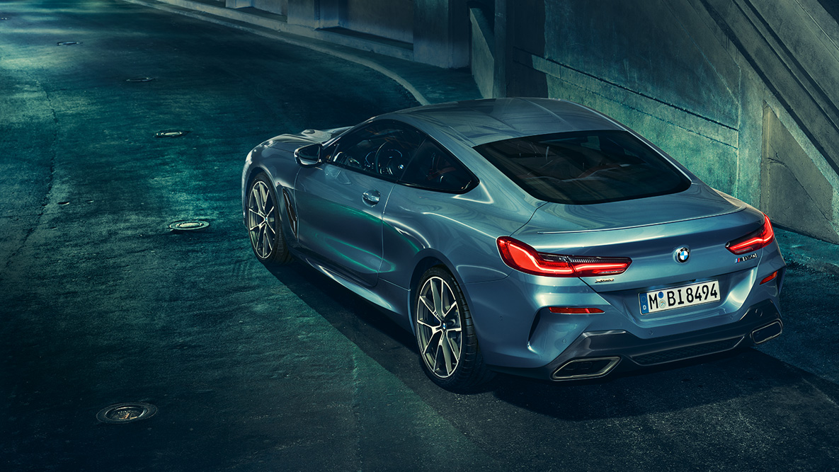 BMW 8シリーズ クーペ、斜めからのリヤ・ショット。 夜の都会を背景にしたBMW 8シリーズ クーペの斜めからのリヤ・ショット。