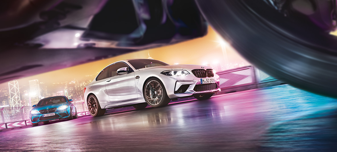 煌めくアスファルトの上に止まるBMW M2コンペティション ローアングルから捉えた夜の街のレーストラックを走る2台のBMW M2 コンペティション。