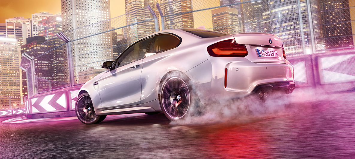 加速するBMW M2 コンペティション 夜のビル群を臨むレーストラックをドリフトするホワイトのBMW M2 コンペティション。