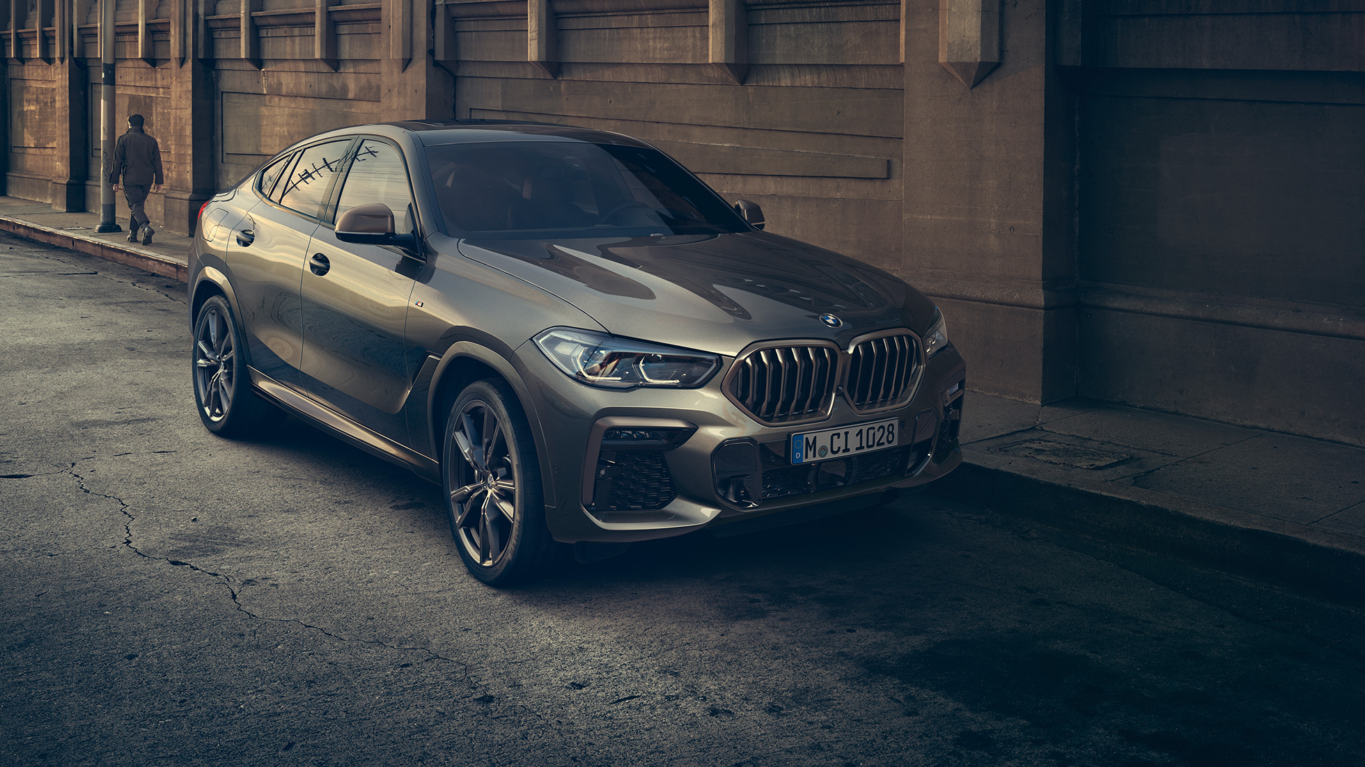 停車中の BMW X6 M50i。G06 市街地を背景に停車する BMW X6 M50i のスリークウォーター・フロントビュー。G06