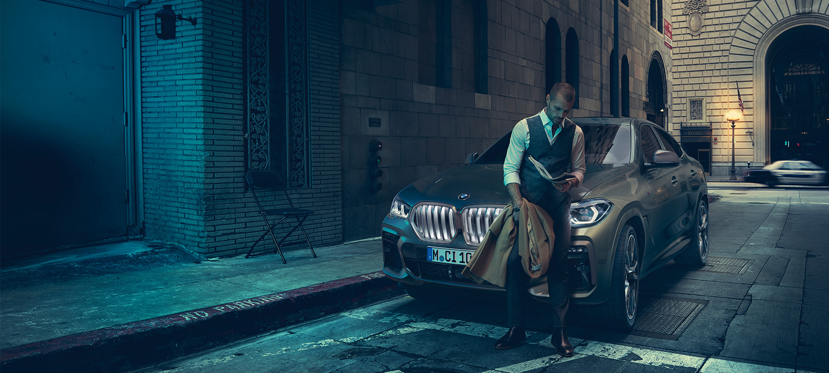 BMW X6 M50i のフロント。 BMW X6 M50i のフロントに寄りかかる男性。