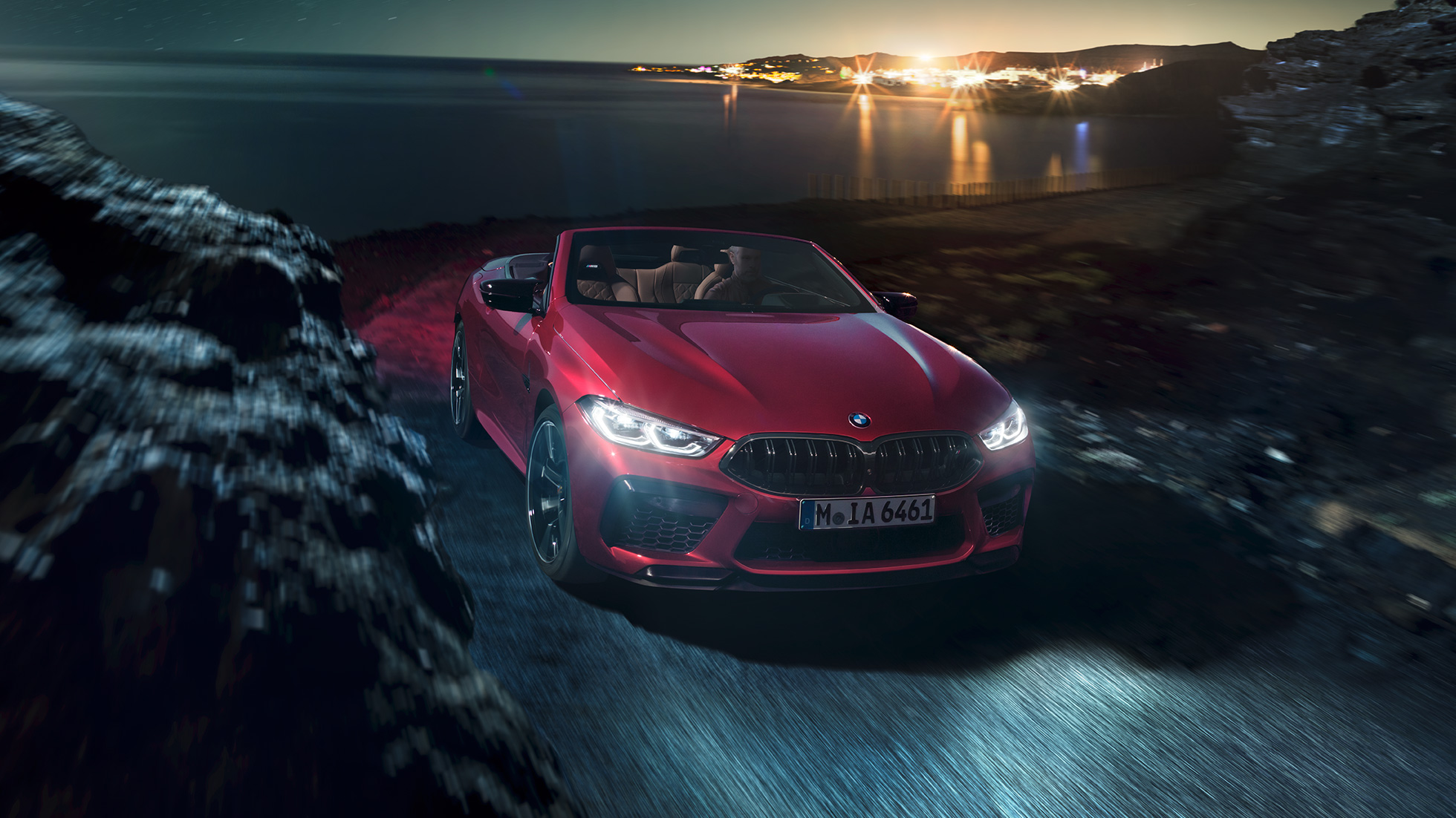 BMW M8 Competition カブリオレ、スリークォータービュー。F91 BMW M8 Competition カブリオレのモテギ・レッド・メタリックカラー (ソフトトップを開けた状態) 、夜の海岸道路上でのスリークォータービュー。F91