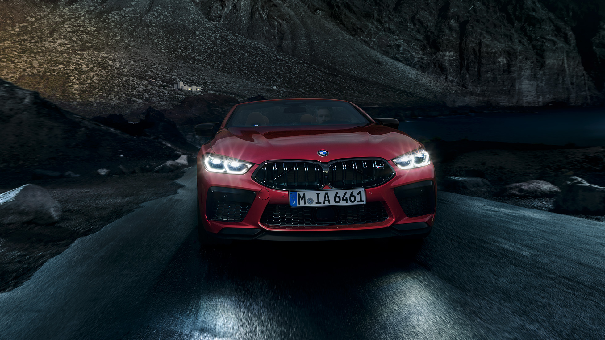 BMW M8 Competition カブリオレ、フロントビュー。F91 ヘッドライトの輝く BMW M8 Competition カブリオレのモテギ・レッド・メタリックカラー、夜間走行中のフロントビュー。F91