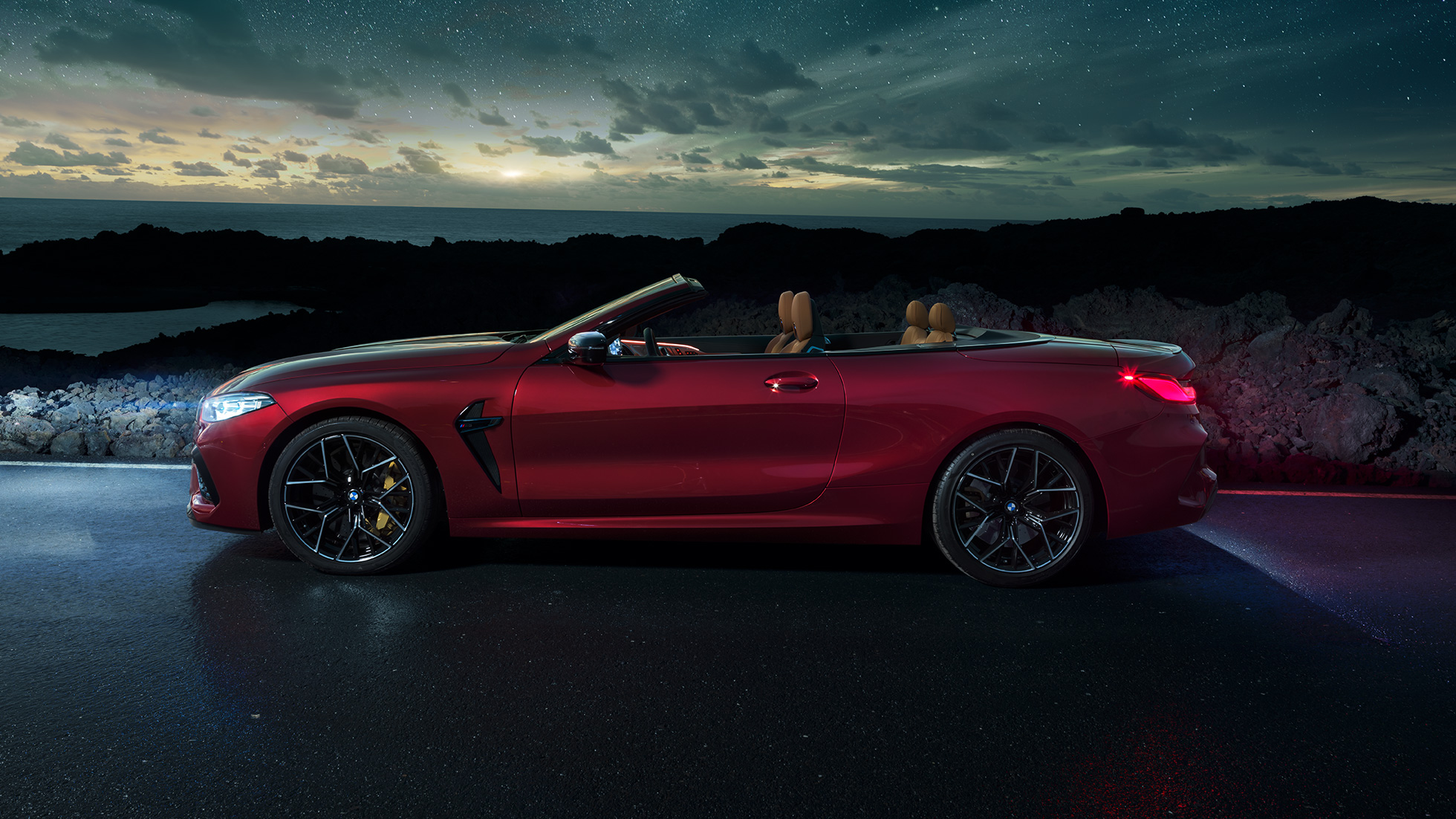 BMW M8 Competition カブリオレ、サイドビュー。F91 BMW M8 Competition カブリオレのモテギ・レッド・メタリックカラー (ソフトトップを開けた状態)、夜の星空の下でのサイドビュー。F91