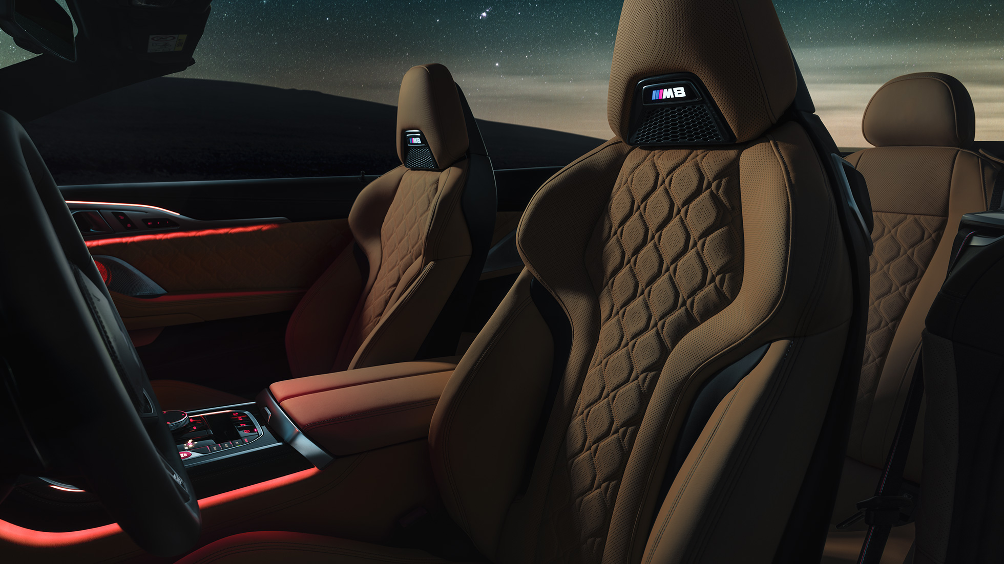 「メリノ」レザー製 M スポーツシート。F91 星空の下の BMW M8 Competition カブリオレ (ソフトトップを開けた状態)、「メリノ」レザー製 M スポーツシートと赤いアンビエントライトを備えたインテリア。F91