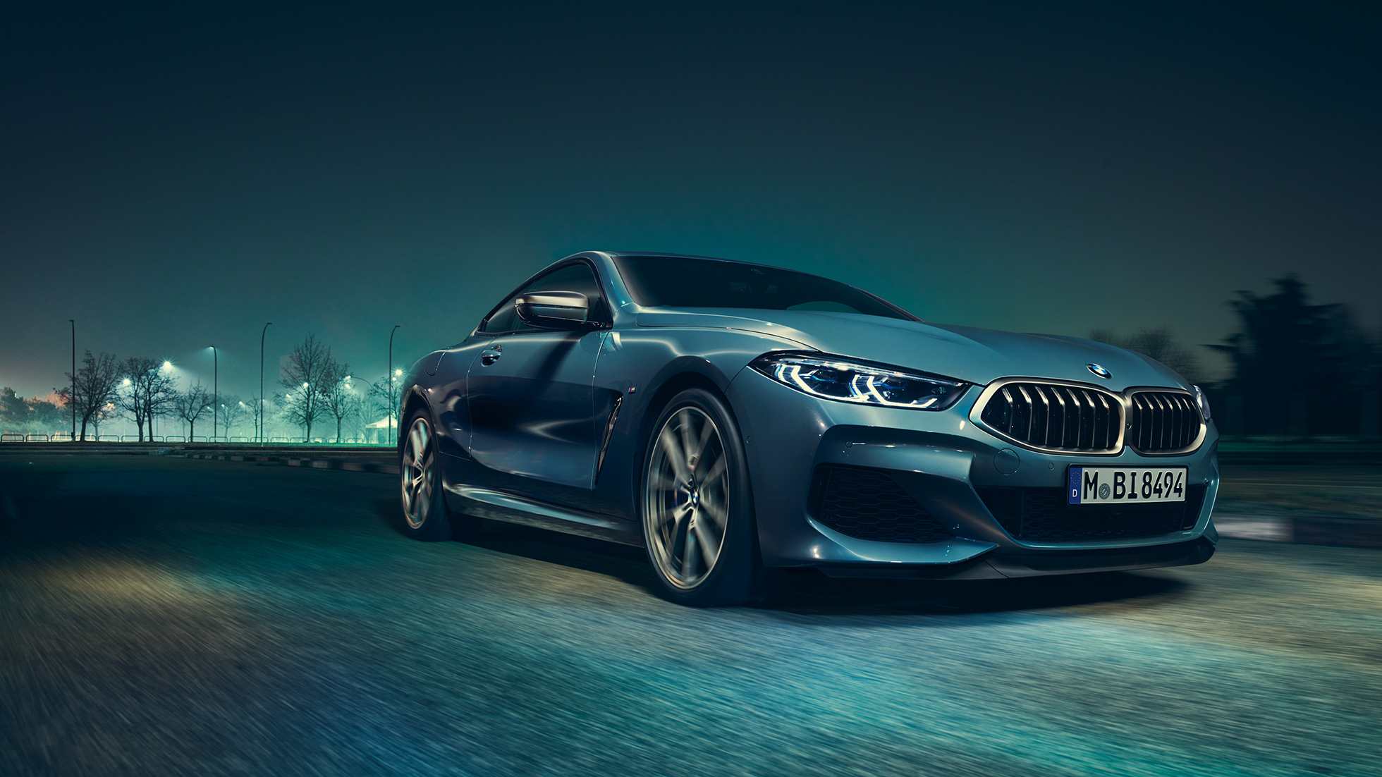 BMW M850i xDriveクーペ、左側から捉えたスリークォーターフロントビュー。G15 BMW M850i xDriveクーペ(塗色バルセロナ ブルーメタリック)。夜間に疾走する車両を左側から捉えたスリークォーターフロントビュー。G15