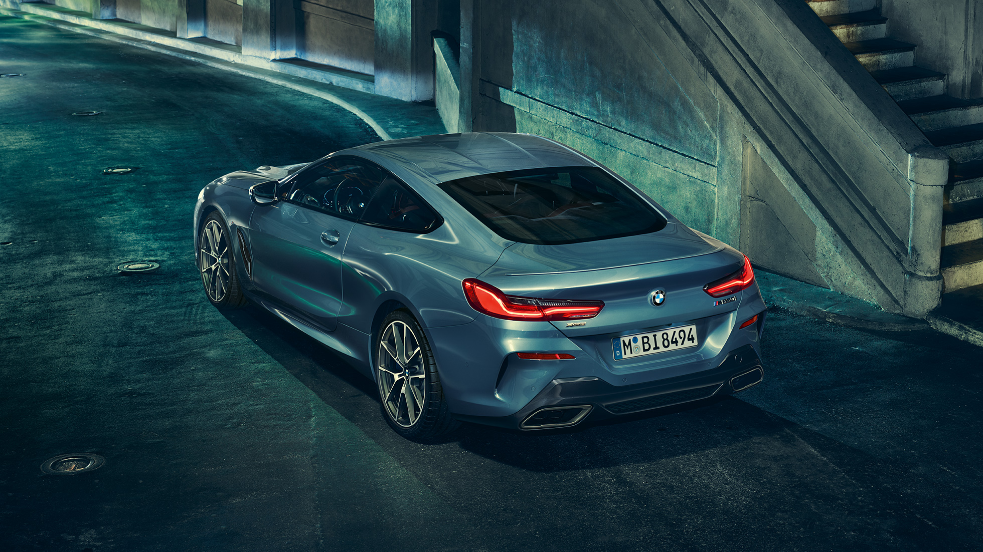 BMW M850i xDrive、左側から捉えたスリークォーターリアビュー。G15 BMW M850i xDriveクーペ(塗色バルセロナ ブルーメタリック)。夜間に停車中の車両を左側から捉えたスリークォーターリアビュー。G15