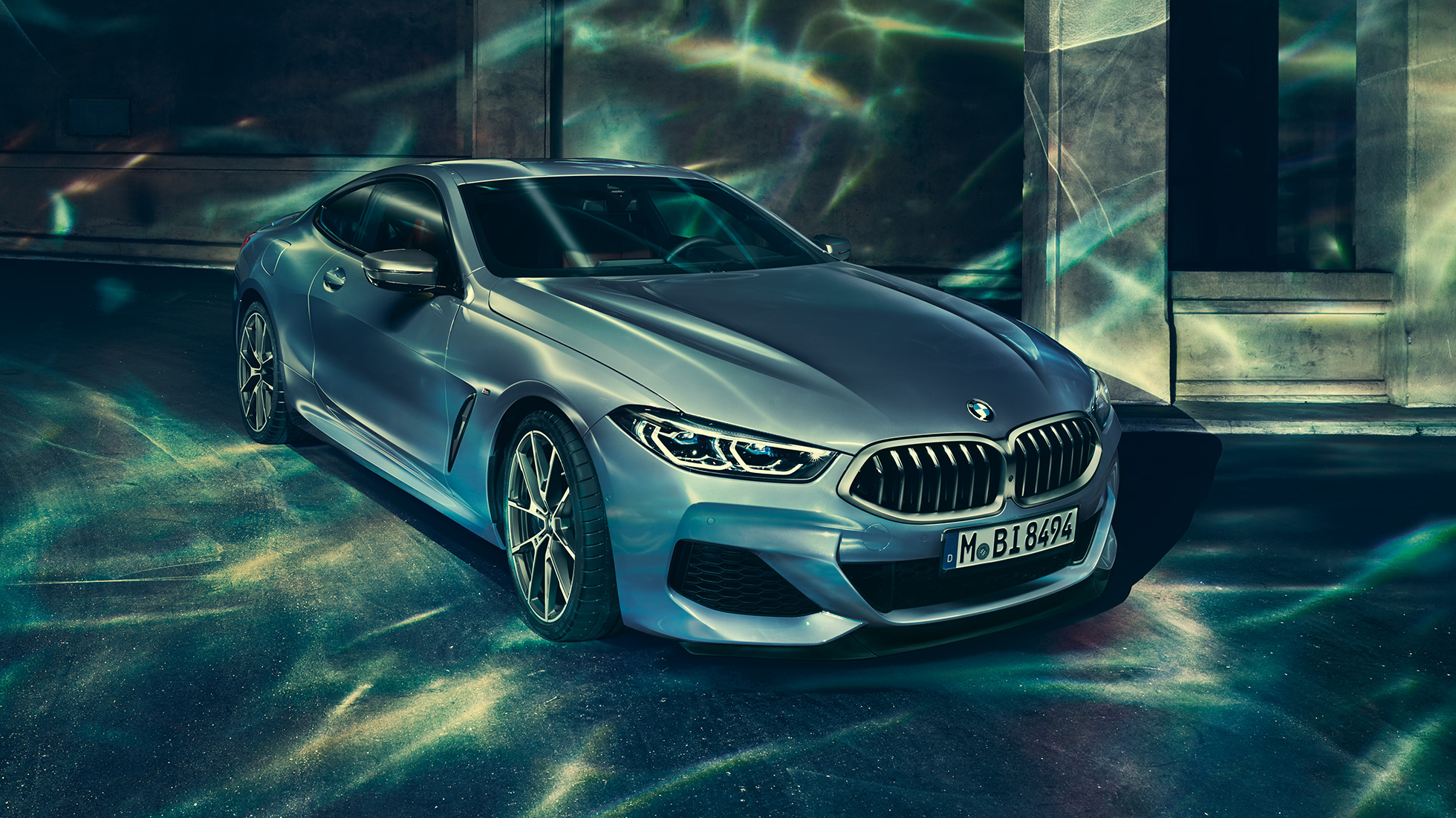 BMW M850i xDriveクーペ、左側からのスリークォーターフロントビュー。G15 BMW M850i xDriveクーペ(塗色バルセロナ ブルーメタリック)。ビルの前に停車した左側からのスリークォーターフロントビュー。G15