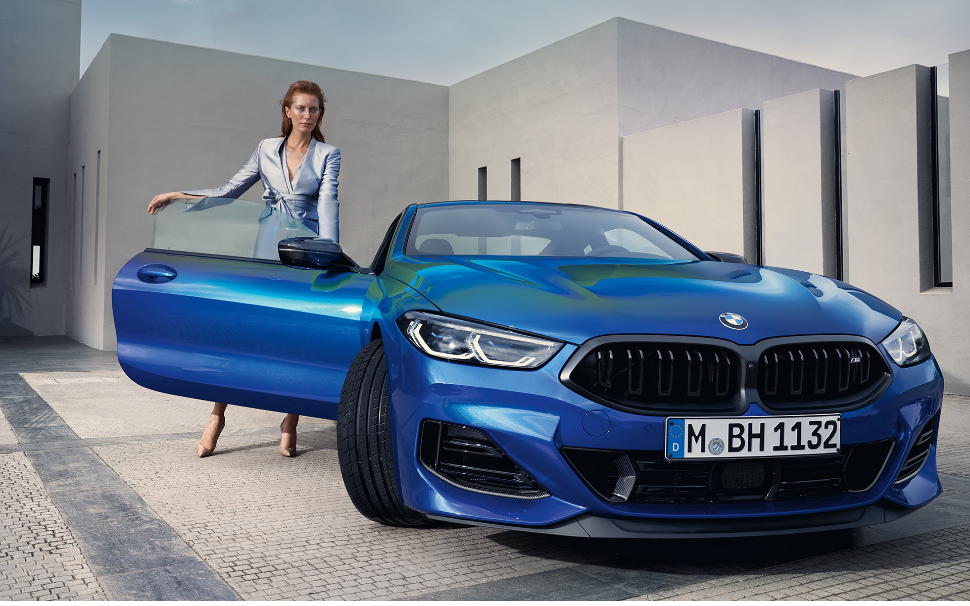BMW M850i xDrive クーペ G15 LCI フェイスリフト 2022 Mポルティマオ・ブルー・メタリック フロント・ビュー 停車中 開いたフロント・ドアのそばにいる女性