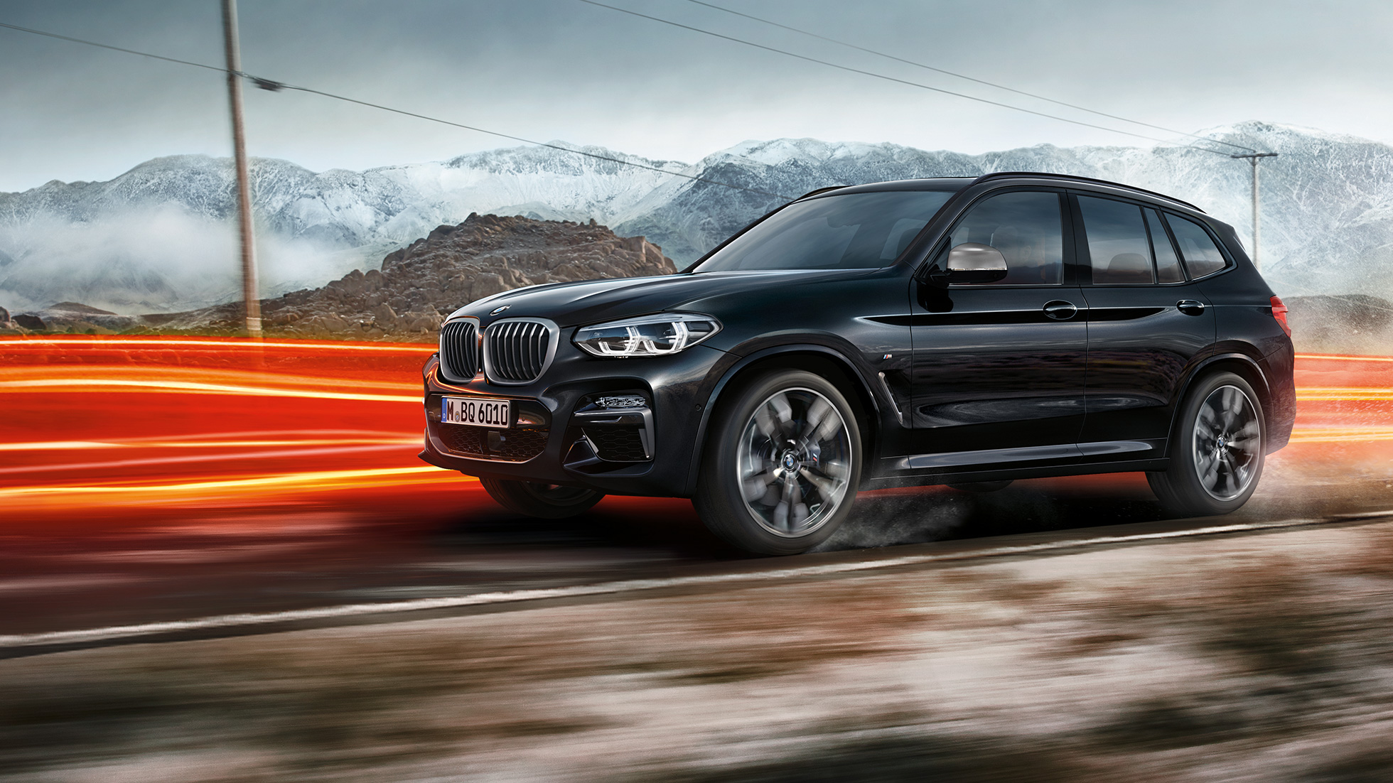 BMW X3 M40d、サイドビュー。F97 BMW X3 M40d のブラック・サファイア・メタリックカラー、走行中、エクステリア、山の風景をバックにライトを点灯させているサイドビュー。F97