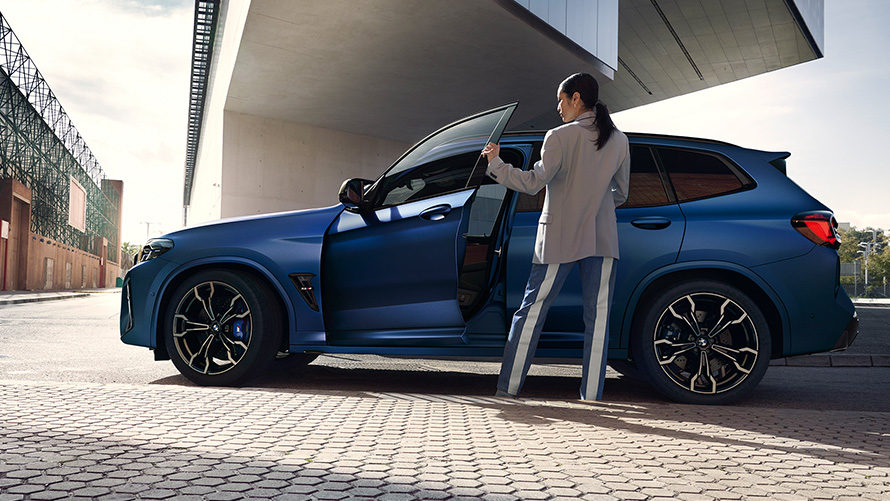BMW X3 M Competition F97 LCI フェイスリフト 2021 フローズン・マリーナ・ベイ・ブルー・メタリック サイド・ビュー ドアを開けた状態で女性モデルとともに