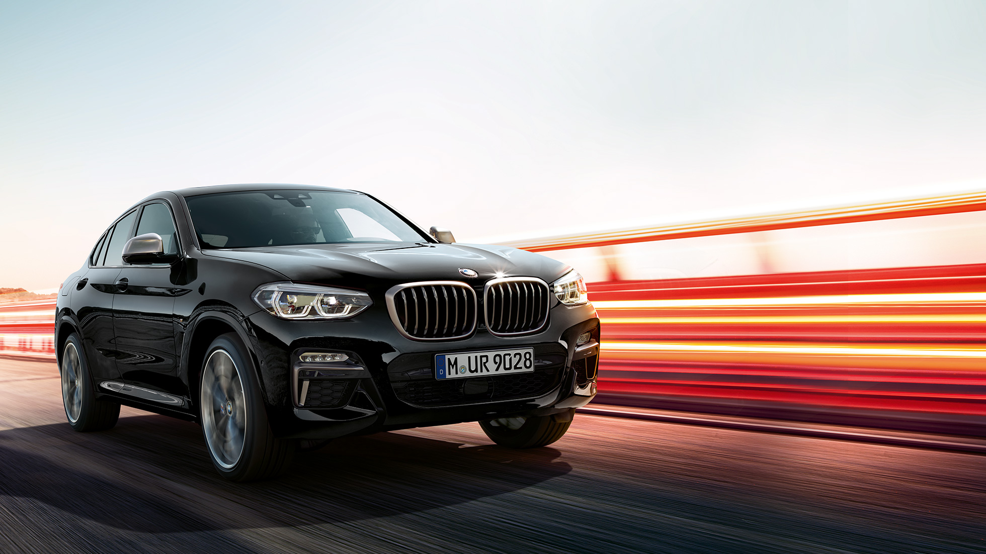 BMW X4 M40i、斜めリア・ビュー。F98 ブラック・サファイア・メタリックのBMW X4 M40i、走行中、エクステリア、ライト・ストリップの見える斜めリア・ビュー。F98