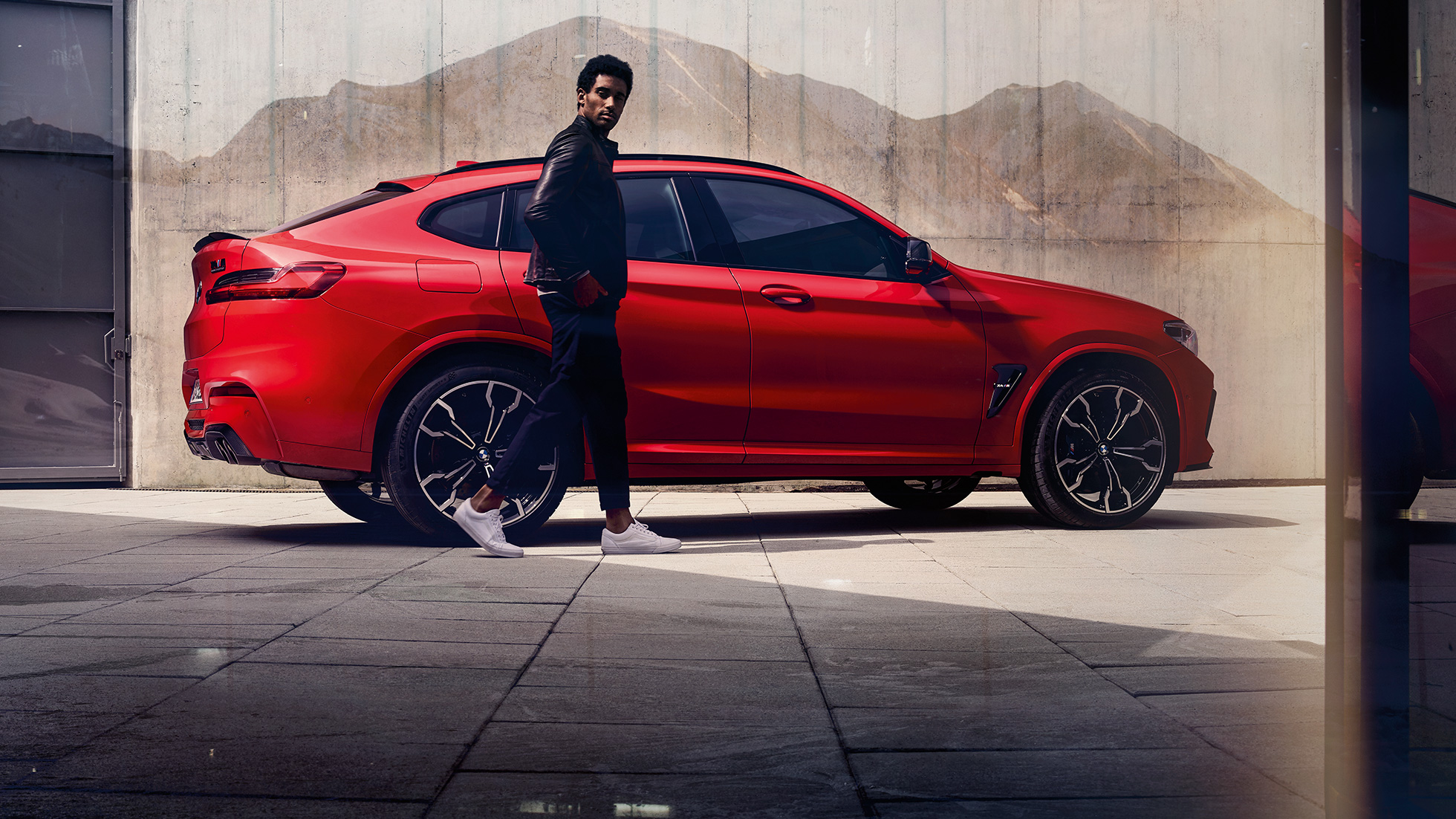 BMW X4 M コンペティション、若い男性が映った側面画像。F98 トロント・レッド・メタリックのBMW X4 M コンペティション、エクステリア、若い男性が映った側面画像。F98