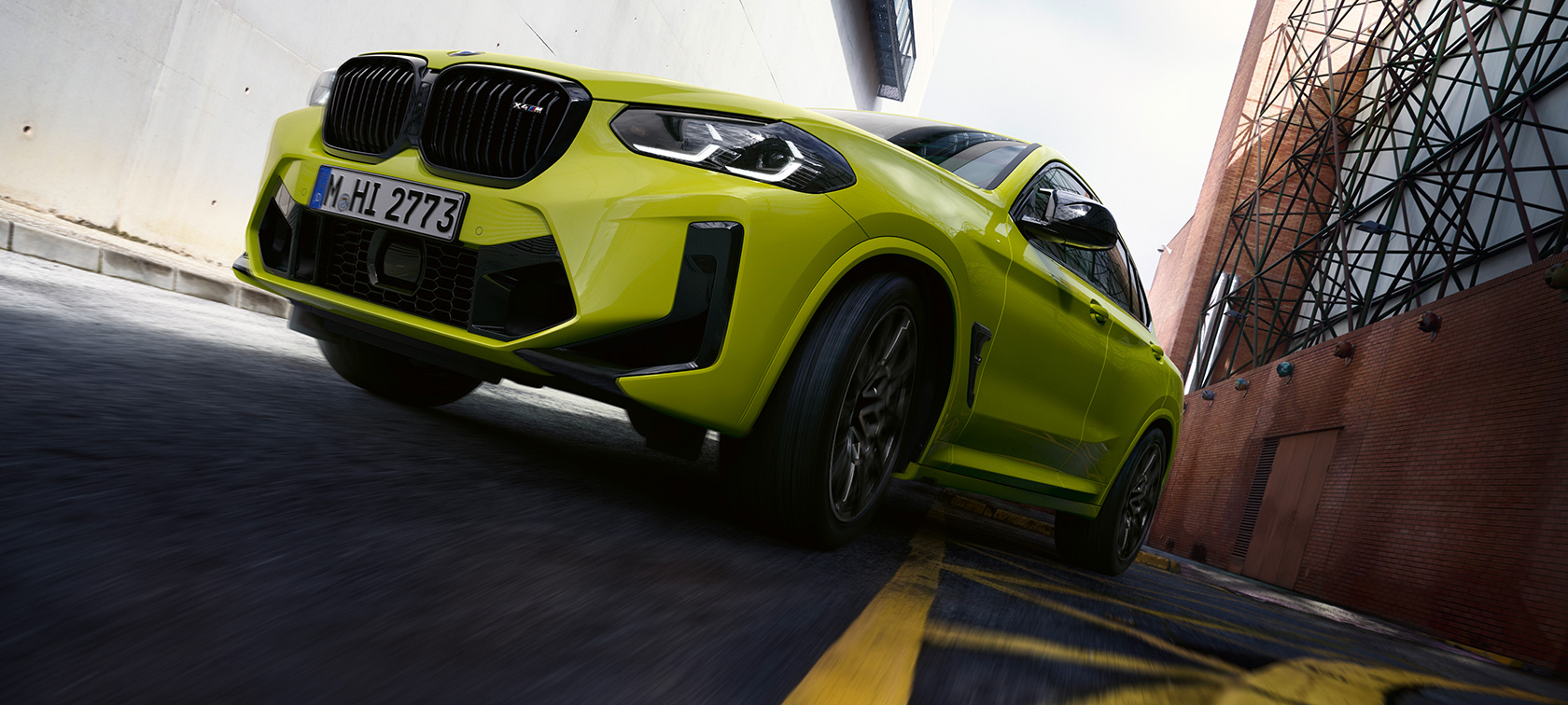 斜めからのフロント・ビューとボトム・ビュー BMW X4 M Competition F98 LCI 2021 BMW X4 M Competition F98 LCI フェイスリフト2021 サンパウロ・イエロー 斜めからのフロント・ビューとボトム・ビュー 家並みの間を走行