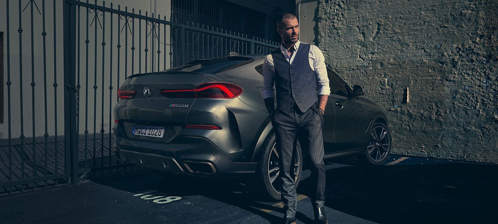 BMW X6 M50i G06、斜めからのリヤ・ビュー BMW X6 M50i G06 2018 SUVの横に立つ男性、斜めからのリヤ・ビュー