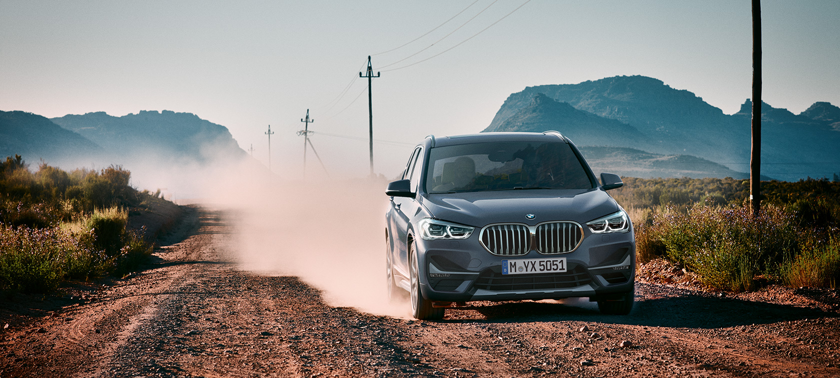 BMW X1、4分の3リアショット。F48 BMW X1、4分の3リアショット、山々の風景の前を走行中。F48