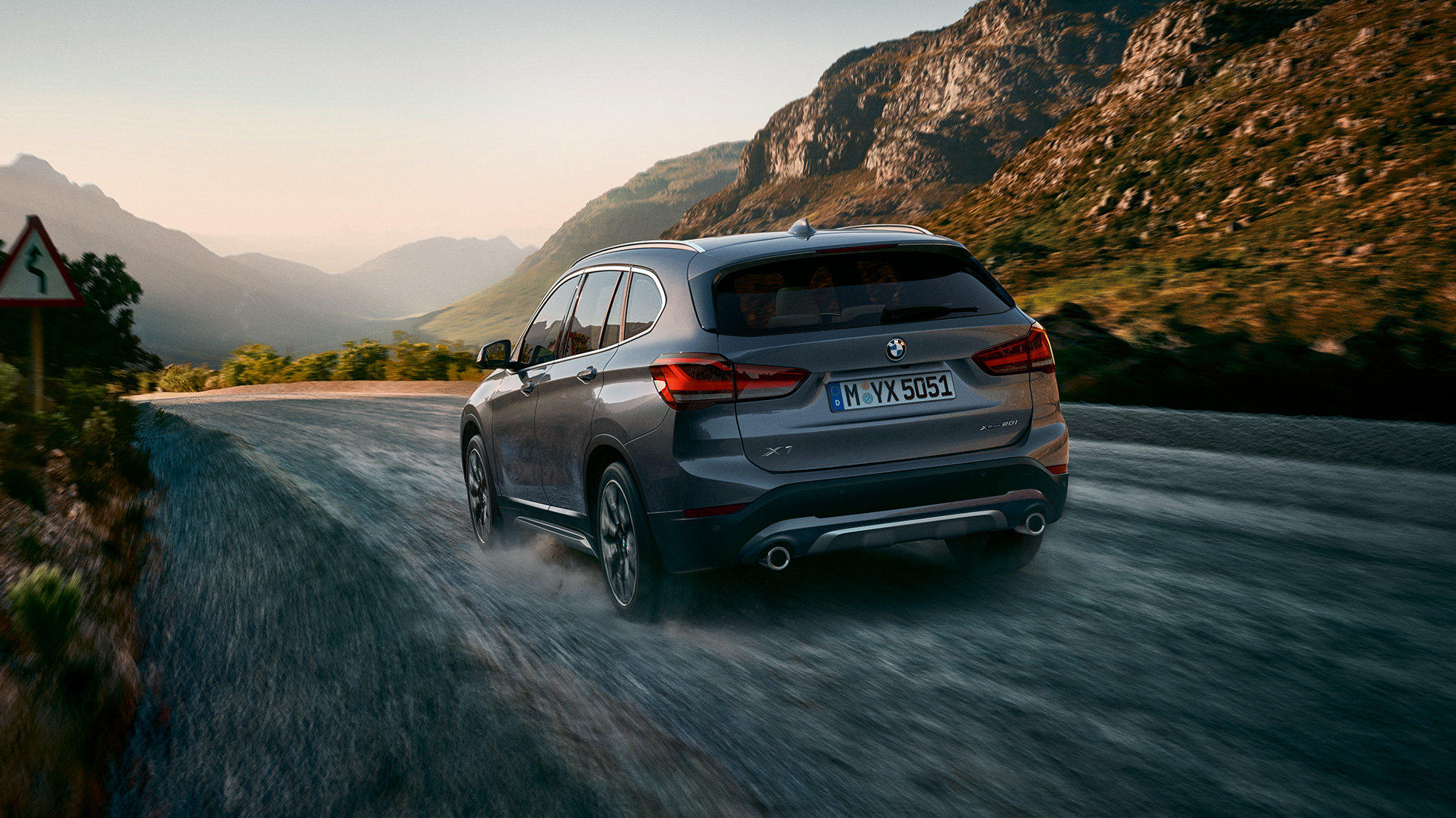 BMW X1、4分の3リヤショット。F48 BMW X1、4分の3リヤショット、山々の風景の前を走行中。F48