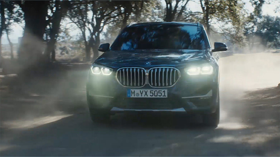 BMW X1 F48 LCI 斜めからのフロント・ビュー BMW X1 F48 LCI 斜めからのフロント・ビュー 自然風景の前を走行中