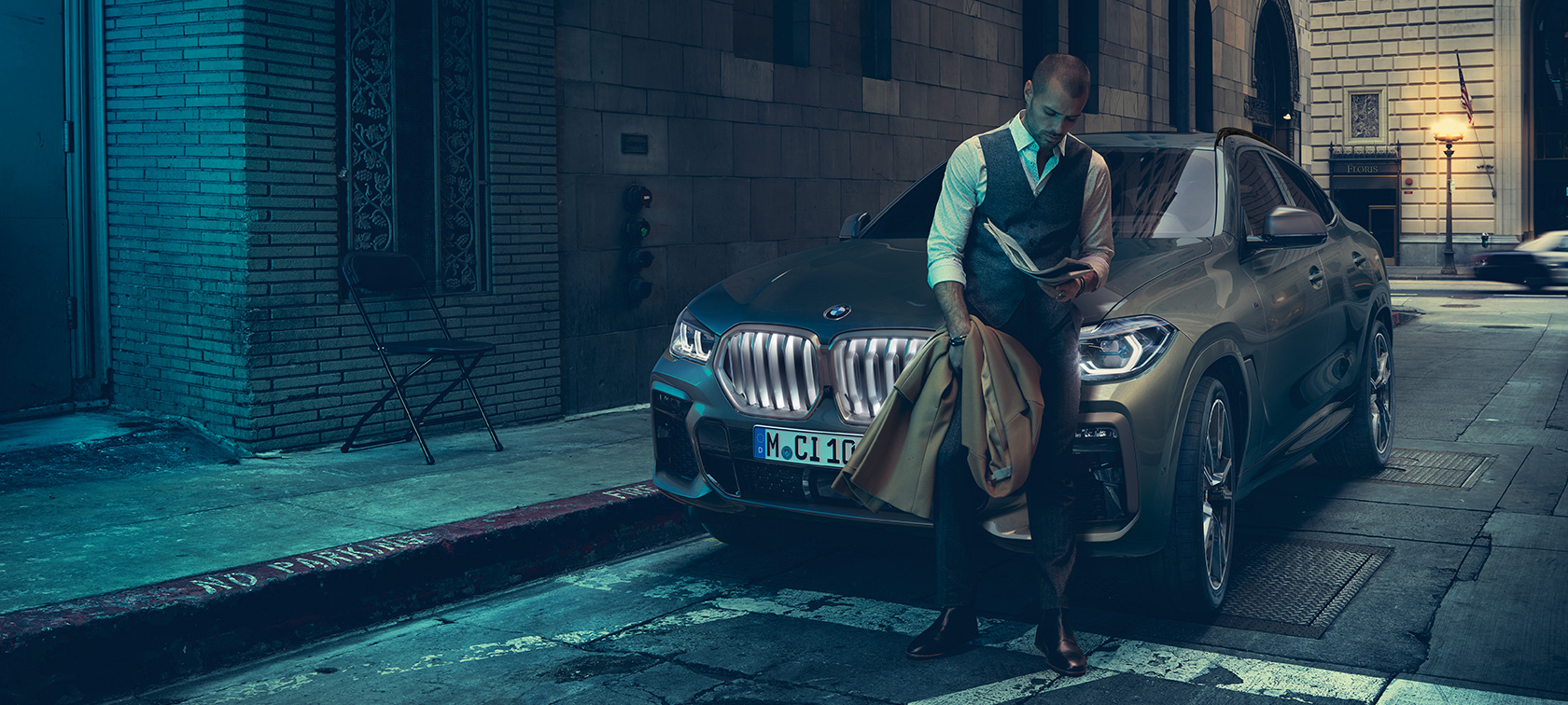 BMW X6に寄りかかる男性。 BMW X6に寄りかかる男性、サイドビュー、ある都市風景を背景に。