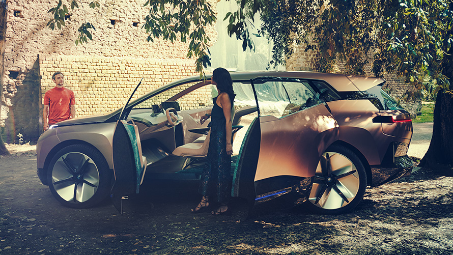 BMW Vision iNEXTの側方からの画像 女性がドアを開け、男性が背景に写るBMW Vision iNEXTの側方からの画像