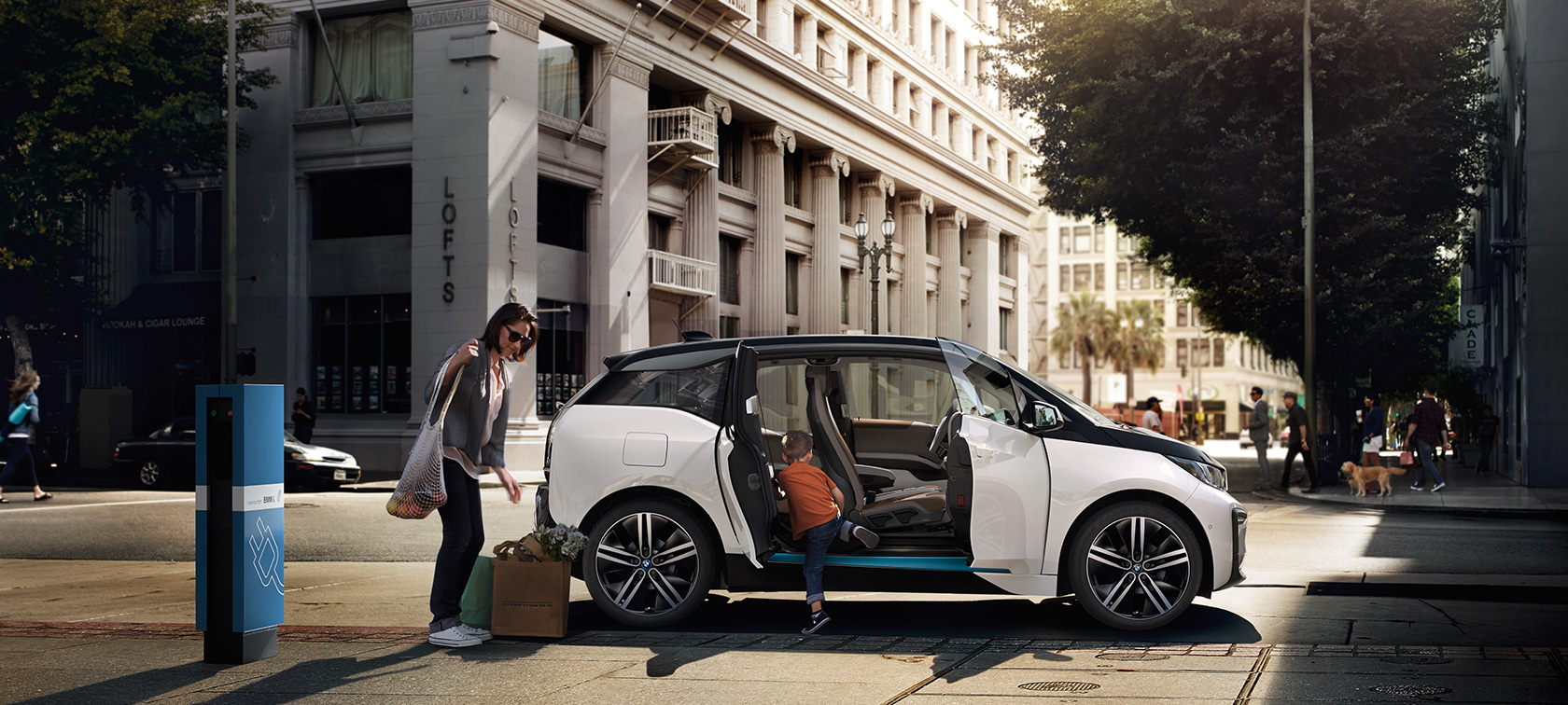 都市を背景に佇むBMW i3 BMW車の航続距離 都市を背景に佇むBMW i3と女性と子供