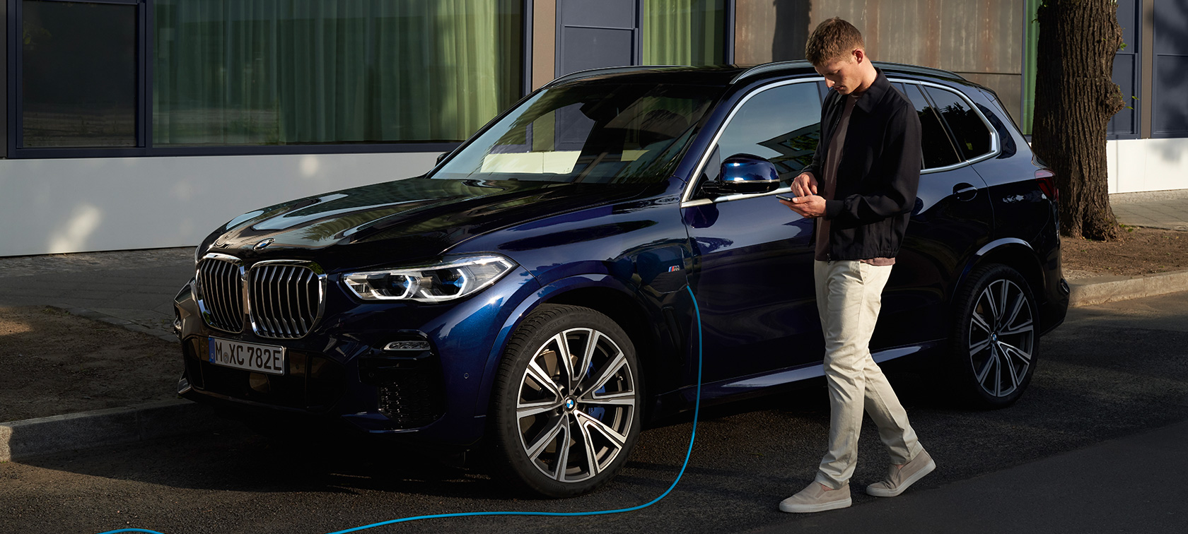 男性がスマートフォンでMy BMW Appを操作 男性がBMW X5プラグイン・ハイブリッドを充電している間にスマートフォンのBMWコネクテッド・ドライブからMy BMW Appを操作