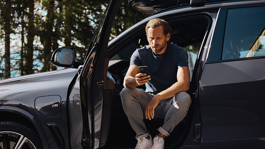 BMW車内に座ってスマートフォンを見る男性 BMW春夏アクセサリー BMW車内に座ってスマートフォンを見る男性
