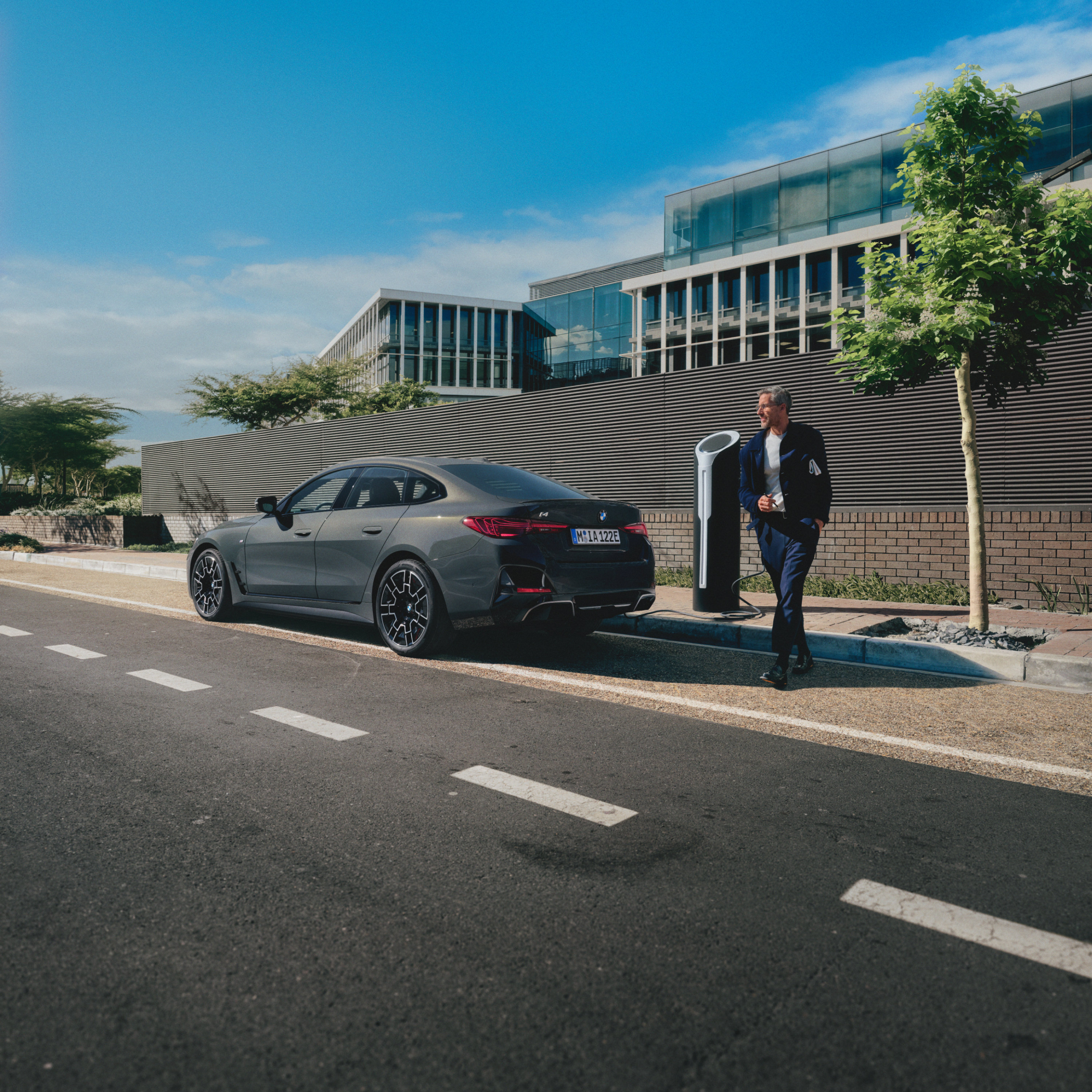 道路の脇で充電中のBMWの背後から歩いていく人